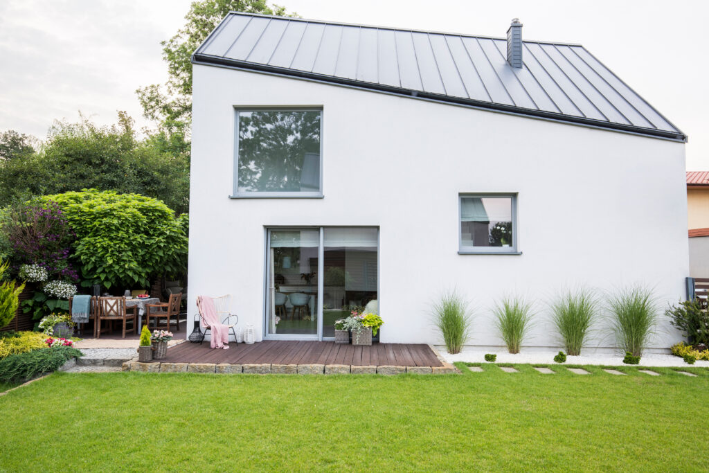 Exterior of a white house with wooden deck, green lawn and bushes in the garden. Real photo