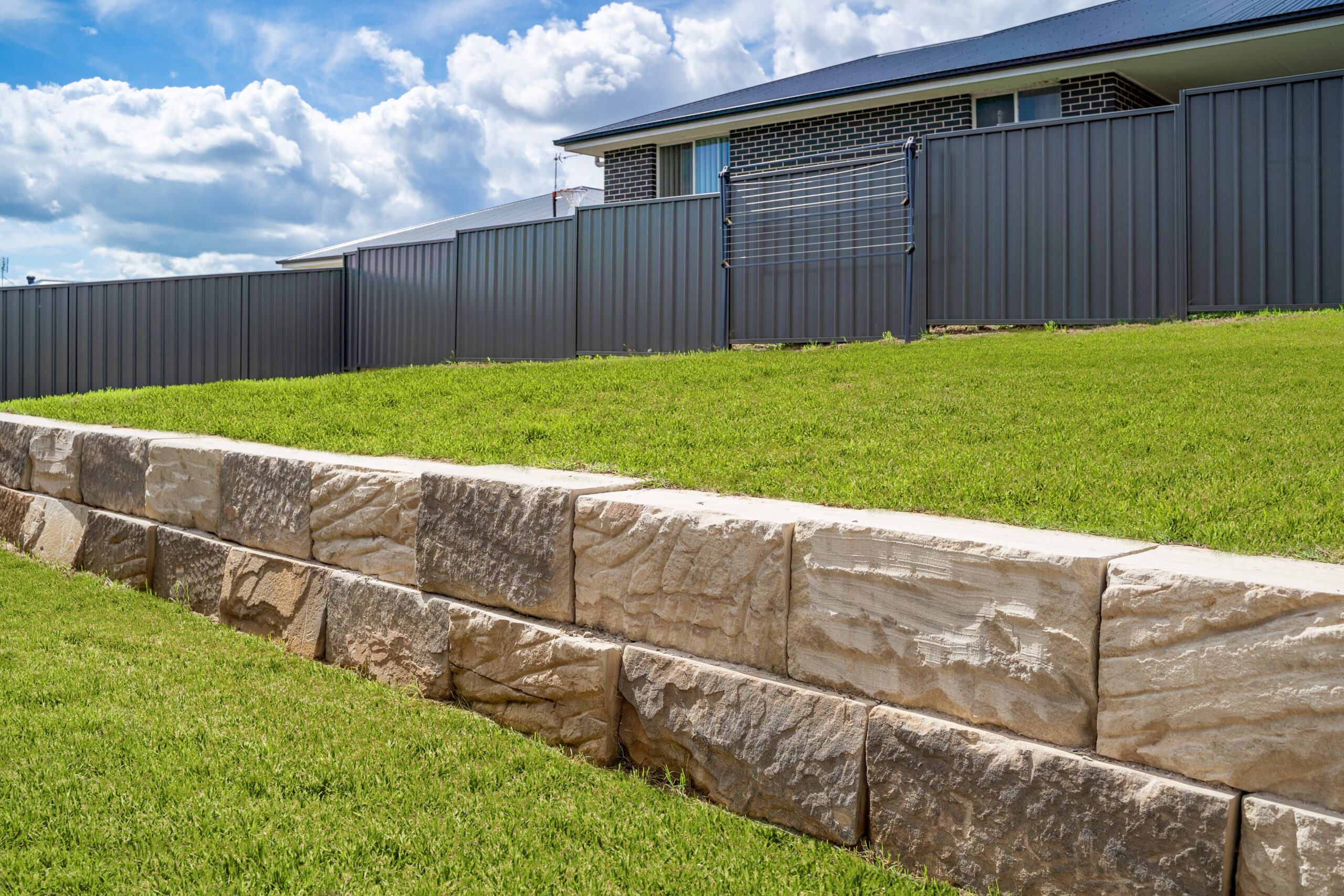 Stone retaining wall backyard green grass fence neighbour