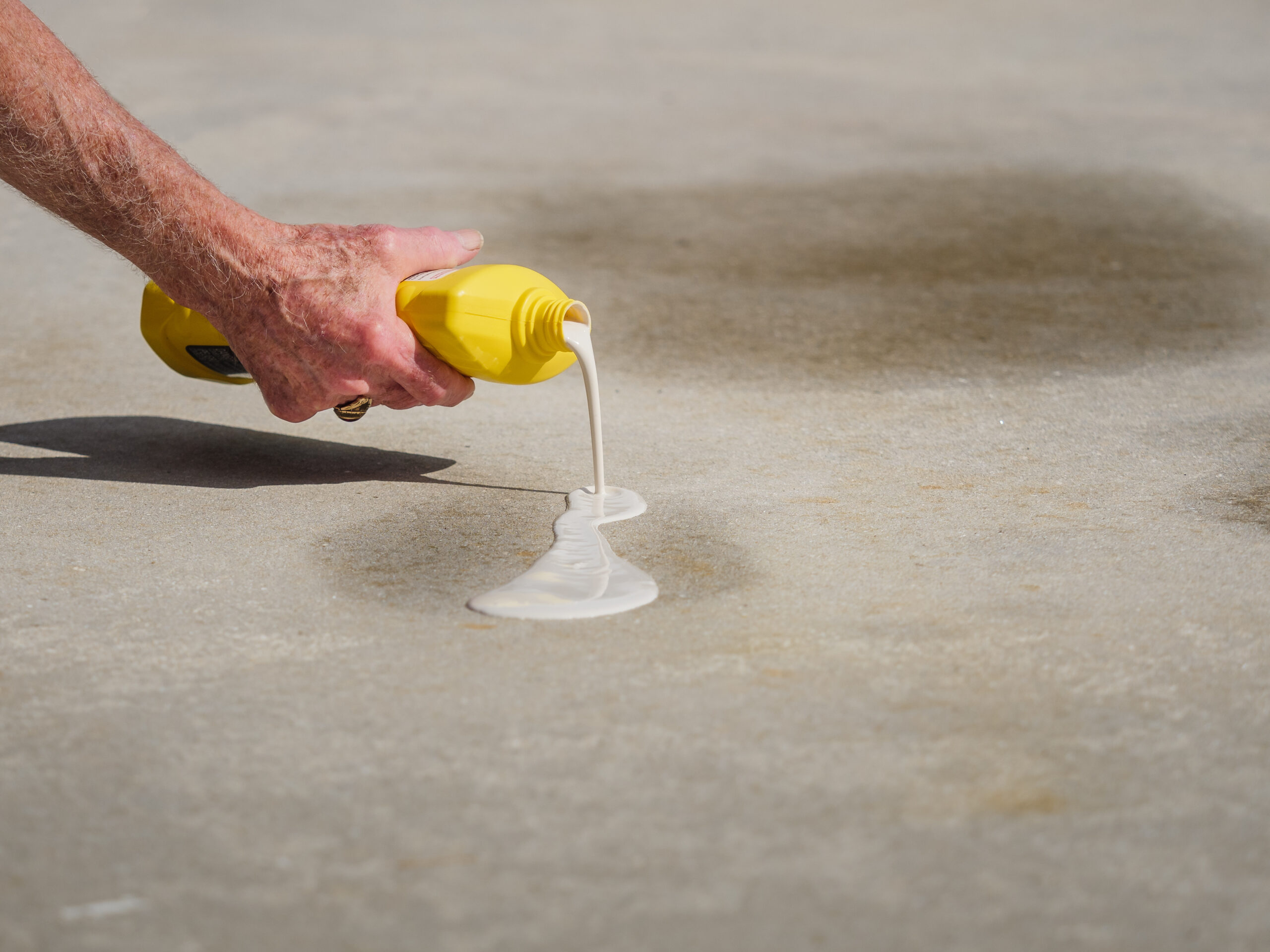 Man applying oil stain remover to concrete driveway. Removing au