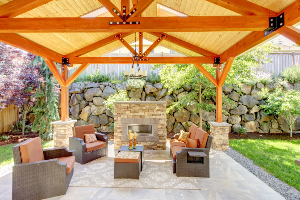 Exterior covered patio with fireplace and furniture. Wood ceiling with skylights.