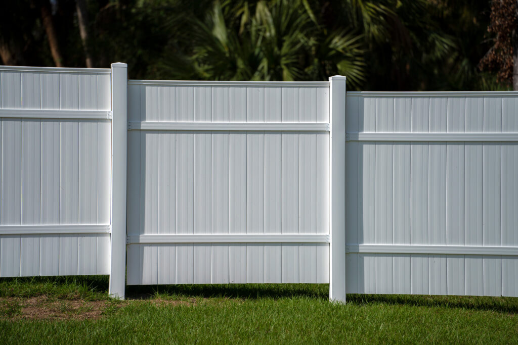 White vinyl picket fence on green lawn surrounding property grounds for backyard protection and privacy.