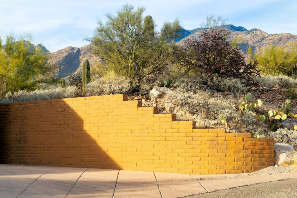 Yellow brick retaining wall wraping around small hill in front yard of house or home in a desert rural community area. In the neighborhood in arizona with native bushes and plants with moutain background.