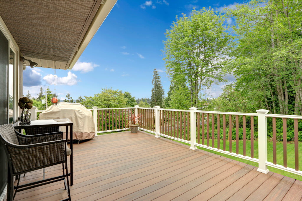 Wooden deck with white and brown railings. Patio table with wicker chairs and barbeque